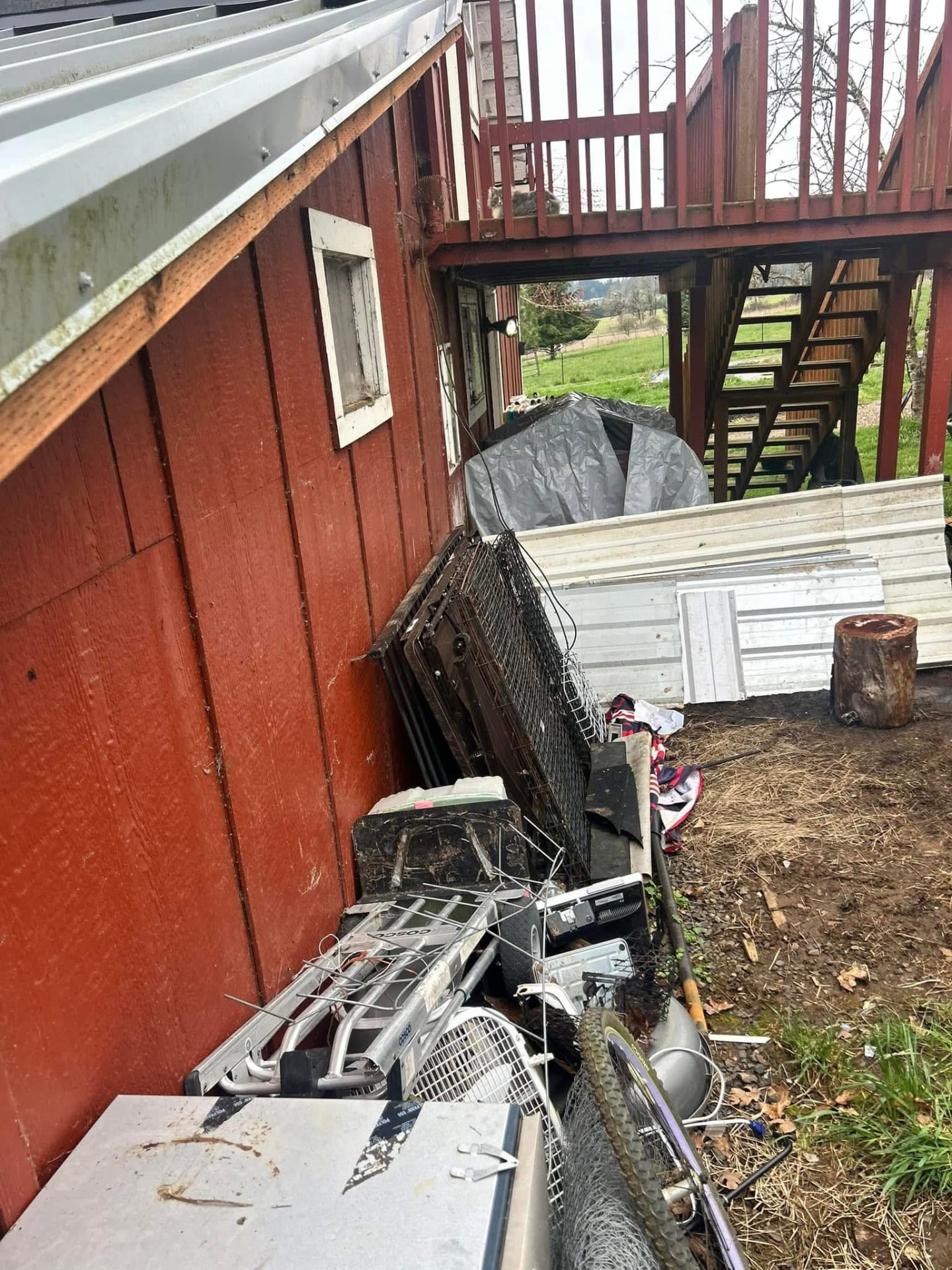 Old appliances, metal panels and scrap piled beside a red outbuilding awaiting removal